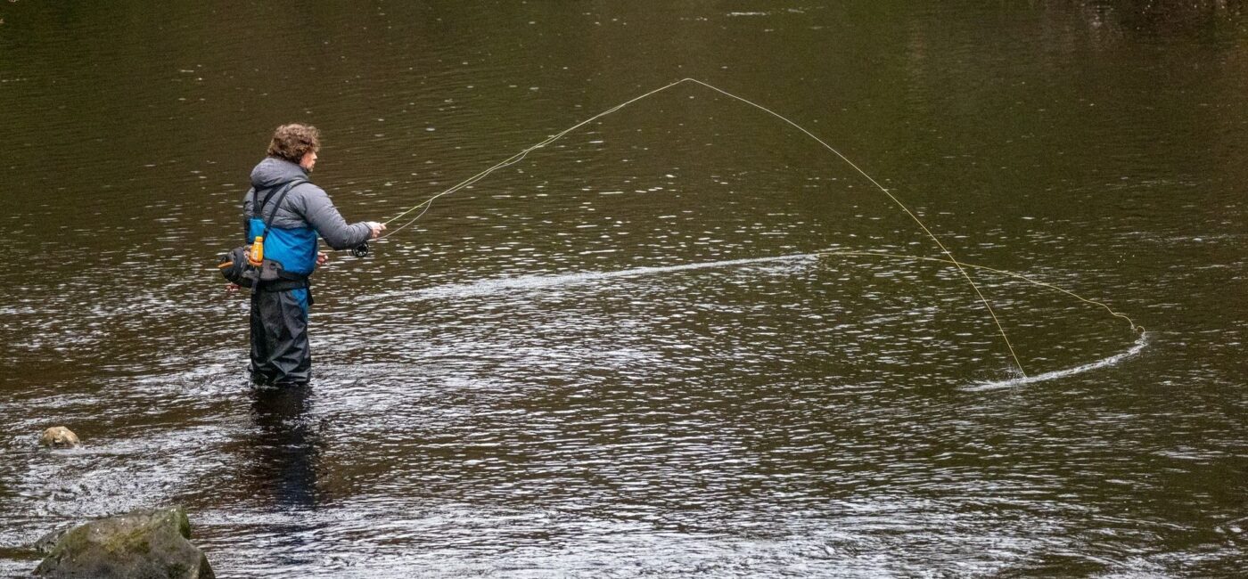 Fly fisher wading through a rocky river pool with line extended