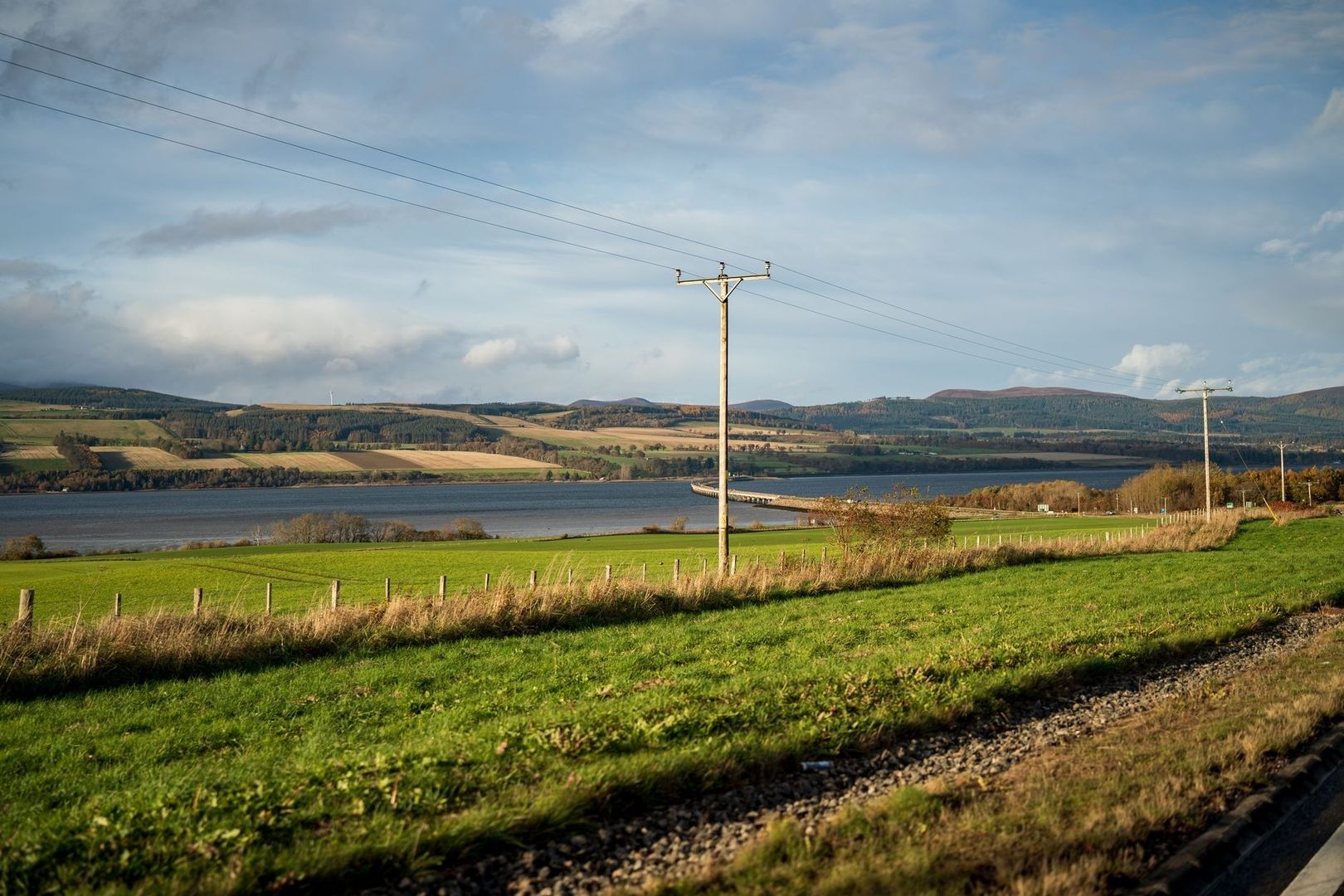 Wide river bordered by farmland, hills, and utility poles in Scotland